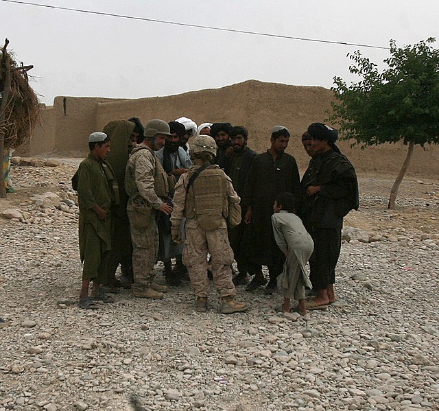 A platoon commander of the 1st Marine Logistics Group, with the battalion interpreter, gather intelligence from local Afghans during a combat logistic