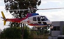 A white, blue, purple, red, orange, and yellow helicopter taking off or about to land