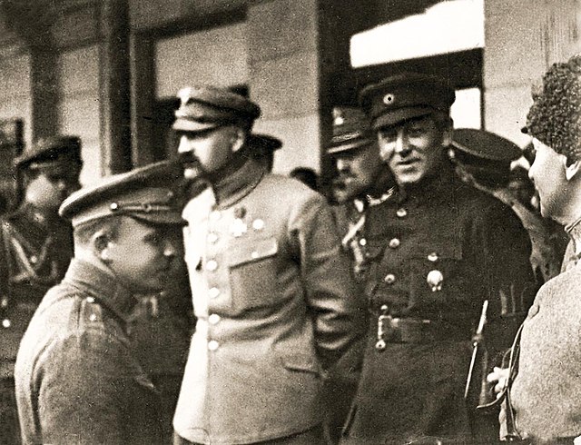 Czarno-białe zdjęcie. Trzy wyraźne postaci żołnierzy. W centralnym punkcie zdjęcia Józef Piłsudski i Symon Petlura