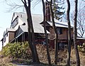 Une grande maison à plusieurs pignons se dresse sur une colline derrière quelques arbres.