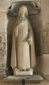 Statue blanche de femme tenant un crucifix avec, à ses pieds, un bouquet de roses