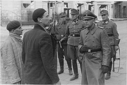 Stroop est à l'arrière, les mains dans le dos, pendant qu'un SS-Sturmbannführer interroge des combattants juifs arrêtés, au premier plan.