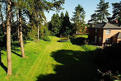 The old station site at Barbers Bridge. The station building is just about visible beyond the pine tree in the centre of the shot: Lots of the trees are recognisable from the 1961 picture. Barbers Bridge station (geograph 4037328).jpg