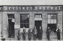 Several men and teenagers stand pose in-front of the printing office.