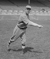 A man in a baseball uniform follows through after throwing a baseball with his right hand.