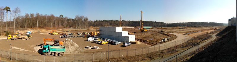 The FAIR construction area from the far east of the GSI ground (spring 2013). On the left, the tree free circle, will give room for the future heavy ion synchrotron SIS100, middle after the container housing two rotary drilling machines (each 100 tons "light") for the approximately 1400 piles, each max 40m deep and appr. 1.2m in diameter, right of the image the place for the future other accelerators and experimental areas. Fair-Baustelle-06-03-2013 panorama-stitch.png