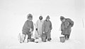 Four people, possibly including Lomen brother(s) and Eskimo woman, filling water buckets from hole cut through ice, Seward (AL+CA 6495).jpg