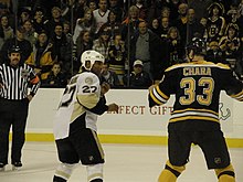 Foto van Georges Laraque en Zdeno Chara met opgeheven vuisten, klaar om te vechten, onder de blik van het publiek en een scheidsrechter.