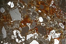 Thin section of rhyolite volcanic rock showing an oxidized iron matrix (orange/brown color). Rhyolite pmg ss 2006.jpg