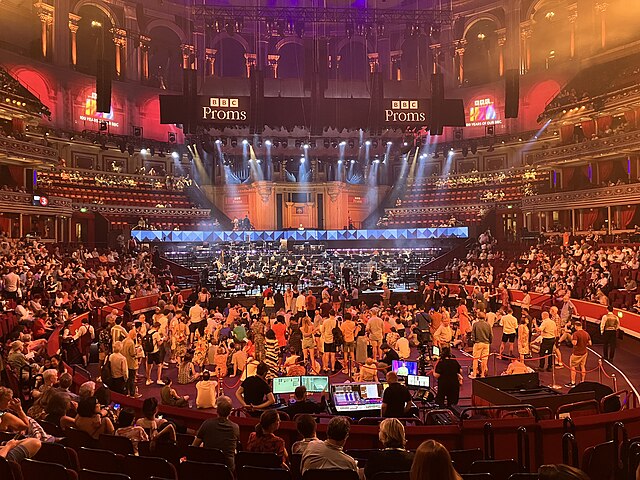 The Proms in 2022. Most people sit, while Promenaders stand in front of the orchestra. The bust of Sir Henry Wood can be seen in front of the organ.