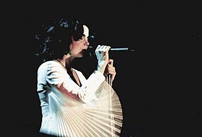 Image d'une femme brune habillée de blanc chantant dans un micro