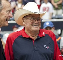 Fotografia de um Phillips rindo vestindo uma camisa pólo do Houston Texans ao lado do ex-presidente dos Estados Unidos George HW Bush