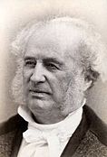 Bust portait photograph of an old man, mostly balded with whispy white hair at the edges of his head and mutton chops, wearing a high collared dress shirt.