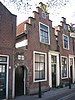 Pand met eenvoudige trapgevel met boven het venster van de zolderverdieping geblokte ontlastingsboog. Deuromlijsting met pilasters en hoofdgestel