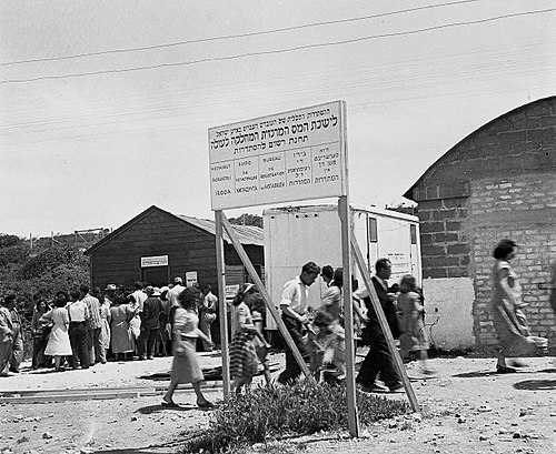 שלט רב-לשוני בכניסה למחנה העולים שער העלייה, 1949. בשלט מופיע מתחת לכיתוב העברי התרגום לשפות הבאות מימין לשמאל: יידיש, לדינו, צרפתית, בולגרית, הונגרית