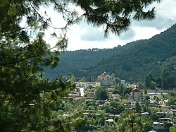 Vista in lontananza della città, con una montagna alberata alle spalle.