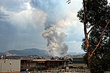 A dark gray plume of smoke rises directly upward from hills in the distance, glimpsed over a middle school campus