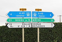 Dos carteles que indican la dirección y el kilometraje de los lugares.  A la izquierda, de arriba a abajo, encontramos la A40 (Ginebra), Bourg-en-Bresse, Polliat y Saint-Cyr-sur-Menthon.  A la derecha, encontramos A40 (París), Mâcon, Vonnas y Replonges.