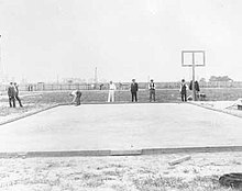 Черно-белая фотография покрытого песком поля в окружении спортсменов и судей