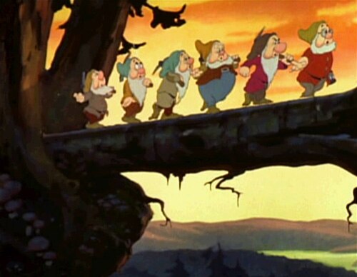 Six out of the seven Disney dwarfs (left to right: Sneezy, Bashful, Sleepy, Happy, Grumpy, Doc) – all but Dopey, who is just off-screen – walking on a