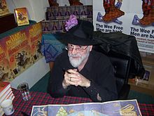 Terry Pratchett, 57 anni, vestito di nero e con un cappello, posa in uno stand.