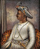 Side portrait of man in turban wearing knitted tunic with gold sword