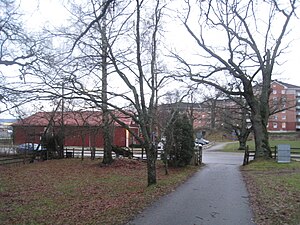 Gården omges av gammal lövträdsvegetation, den stora ekonomibyggnaden i bakgrunden är logen.