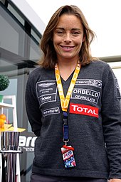 A woman in her mid-30s wearing green clothing with sponsors logos and smiling at the camera