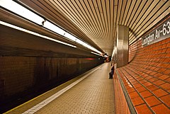 Lexington Avenue–63rd Street station platform, dengan kereta bawah tanah jalur di sebelah kiri, krem platform ubin, dan jeruk dinding palsu di sebelah kanan