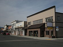 A small, two-story building with a sign for "Arlington Hardware & Lumber" facing a city street, joined by similar-sized buildings with business of their own.