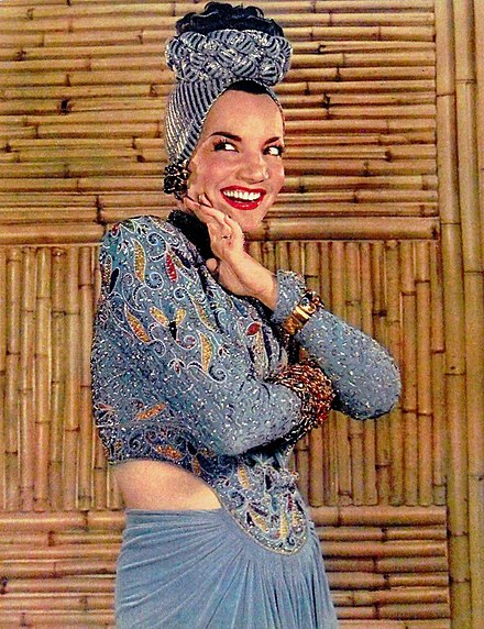A smiling Carmen Miranda against a bamboo wall