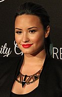 A woman with red lipstick and long hair dark poses on a red carpet.