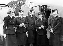 Photo noir et blanc de cinq femmes en uniforme (trois ont un calot, une porte une casquette) posant devant un avion.