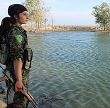 A YPJ soldier next to a large reservoir in Northern Syria Kurdish YPG Fighter (23306158716).jpg