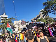 2024 LGBTQIA March in Curitiba, with Pride flags and a man holding a Palestinian flag and slogan "From the River to the Sea" in Portuguese