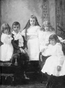 Fotografía de grupo en blanco y negro de 4 niñas con vestidos blancos y un niño con traje.