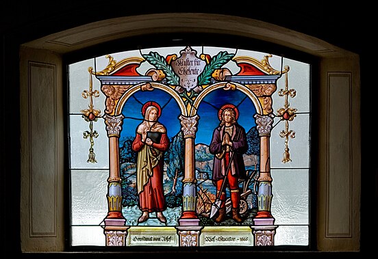 Muster für Eheleute (“modelo para casados”), vitral criado em 1885 pelo mestre de estuque Josef Rief na igreja paroquial de Nossa Senhora da Assunção em Nesselwängle, Tirol, Áustria. O vitral retrata o casal de santos, Maria Toribia e Isidoro, o Lavrador. Apesar dos séculos que se passaram, Isidoro e Maria continuam a ser fortes exemplos do significado vocacional do matrimônio, não apenas como uma instituição que atende a uma necessidade de afeto ou de continuar uma linhagem familiar, mas também como uma vocação por meio da qual as pessoas podem alcançar a santidade. (definição 3 564 × 2 446)