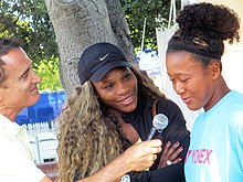 A reporter holding a microphone to Osaka with Williams to the side smiling