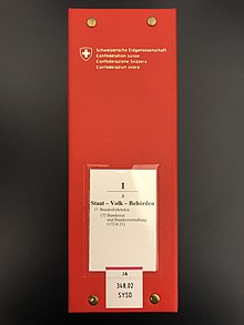 Photographie de la tranche d'un classeur rouge avec étiquette blanche concentrant le volume 1 du Recueil systématique en langue allemande