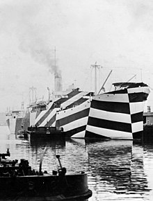Ein Kriegsschiff, das mit einem wilden Muster aus schwarzen und weißen Streifen lackiert wurde. Die Konturen des Schiffes sind nicht mehr zu erkennen.