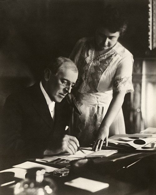 U.S. President Woodrow Wilson's first posed photograph after his stroke, with First Lady Edith Wilson holding a document steady while he signs.