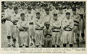 A black and white photograph of seventeen standing on a baseball field wearing light baseball uniforms with dark stripes and caps.