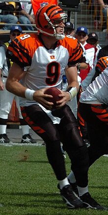 Carson Palmer in a Bengals jersey and helmet scrambling with a football in his hands.