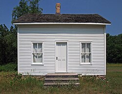 Tiny gabled house with clapboard siding and two windows flanking a central door