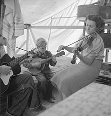 Woman playing fiddle (right) with her family in a California migrant camp, 1939 HillbillyFamilyBandDLange.jpg