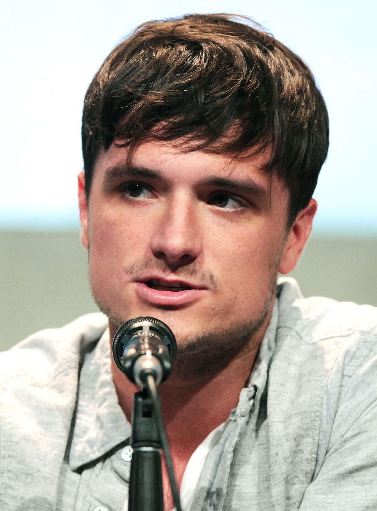 Josh Hutcherson smiling, wearing an open patterned brown and tan flannel, with a brown shirt underneath