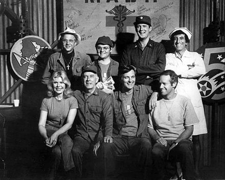 Cast photo from M*A*S*H for 1977: Front row from left – Loretta Swit, Harry Morgan, Alan Alda, Mike Farrell. Back row from left – William Christopher, Gary Burghoff, David Ogden Stiers, and Jamie Farr