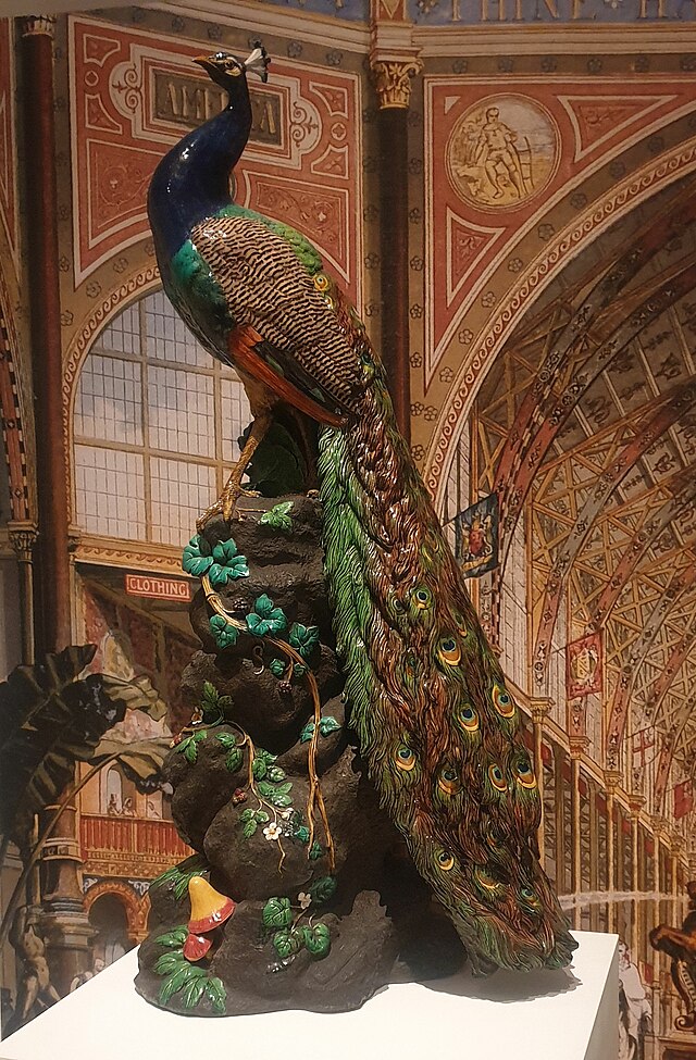 A naturalistic and life-sized model of a peacock, posed on a rather fantastical mound decorated with mushrooms