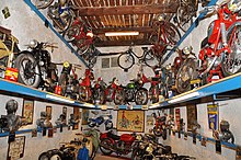 Petite pièce à poutres au plafond : des moteurs et des motos sur trois rangs sont accrochés au mur.