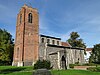 Een kerk gezien vanuit het zuidwesten met een grote bakstenen toren aan de linkerkant en het vuurstenen lichaam van de kerk aan de rechterkant, met de lichtbeuk, zuidbeuk en veranda